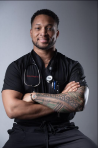 Photo of Emeka sitting on a stool wearing black scrubs.