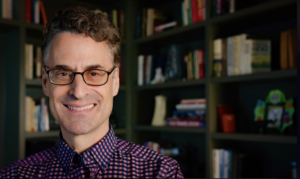 Photo of Edward Burger smiling while standing in front of a bookshelf. 