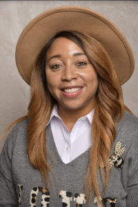 Photo of Kerrie smiling wearing a hat with gray sweater and white shirt underneath. 